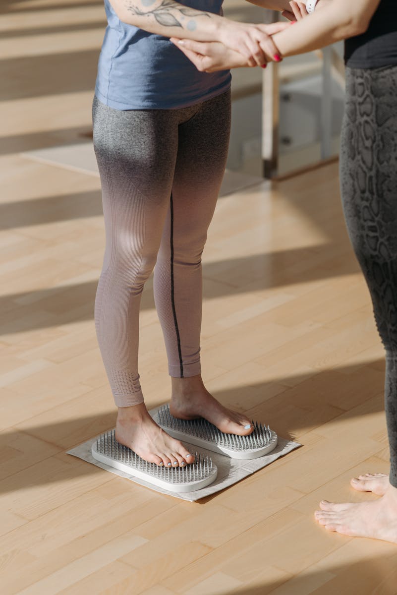 Two women engage in acupressure with foot mats indoors, promoting wellness.