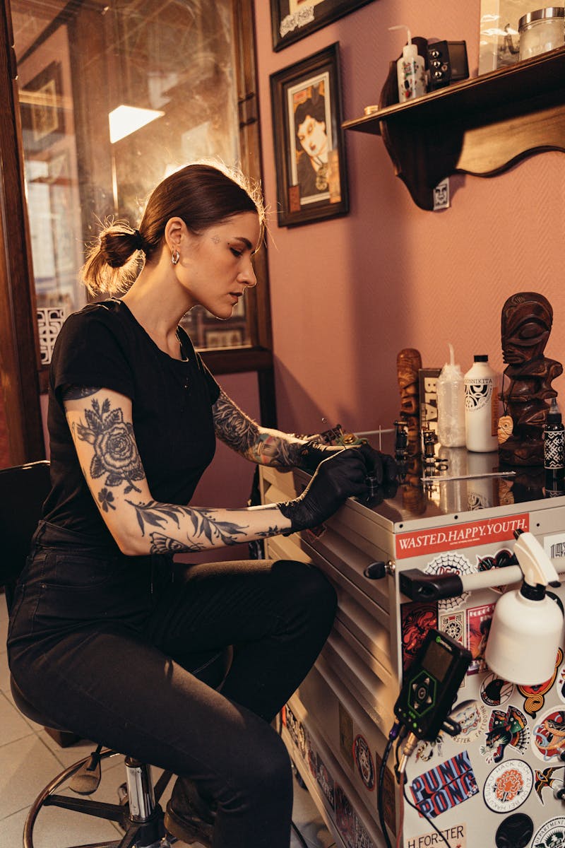 A tattoo artist concentrating on her work in a warmly decorated studio, surrounded by art pieces.